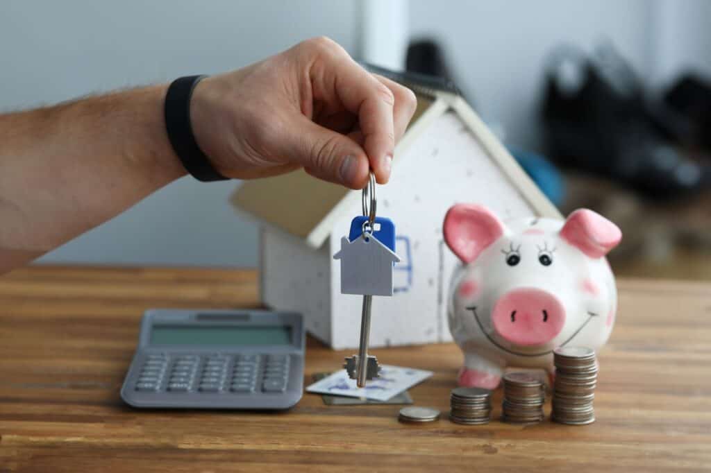 A calculator, house figurine, coins, house key, and piggy bank in the concept of cost of relocation