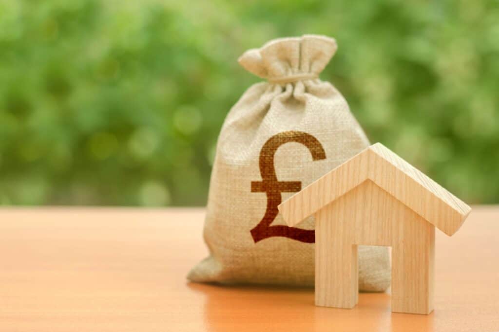 A wooden house figurine and pound sterling money bag in the concept of house move costs