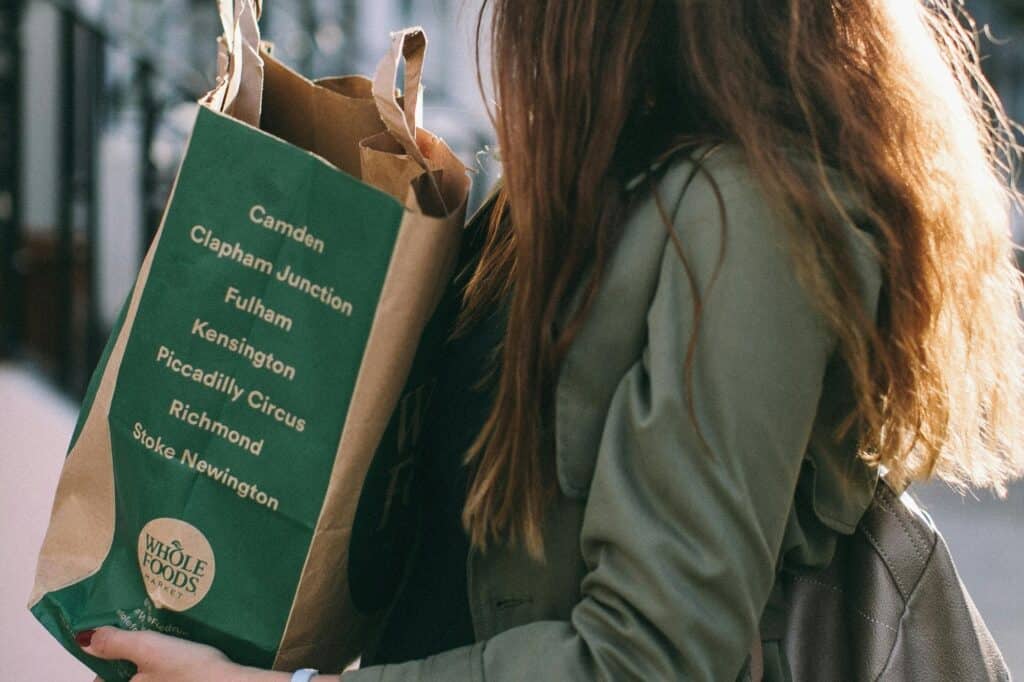 A woman is holding a paper bag from a local shop of whole foods